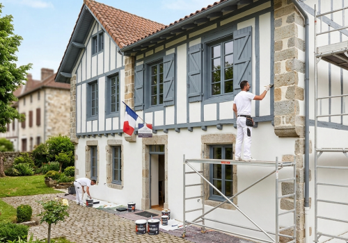Artisan Peintre à Orthez : Artisan peintre de Peinture 40-64 réalisant le ravalement de façade d'une maison béarnaise traditionnelle à Orthez, avec mise en peinture moderne des boiseries en gris ardoise.